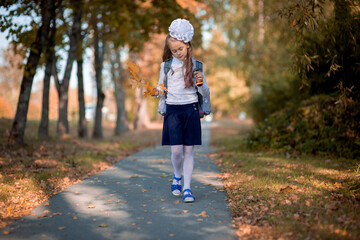  schoolgirl with a school bag on her back walking in autumn park