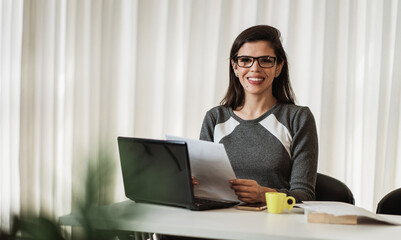 Young beautiful Brazilian woman working with laptop while sitting at office desk, working from home concept.