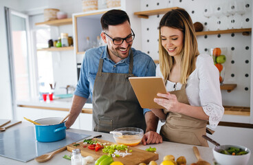 Happy young couple enjoys and having fun preparing healthy meal together at home kitchen.