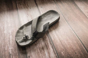 An old damaged flip flop on the floor. Toe post torn and ripped off by a dog. Copyspace.
