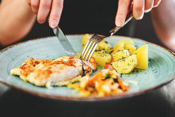 woman hand holding fork and knife eat chicken breast meat with potato in a plate