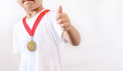 A happy teenage boy-dressed in a gold medal, smiles and gives a thumbs up to the camera, standing isolated against a white background. selective focus. the concept of sports and victories