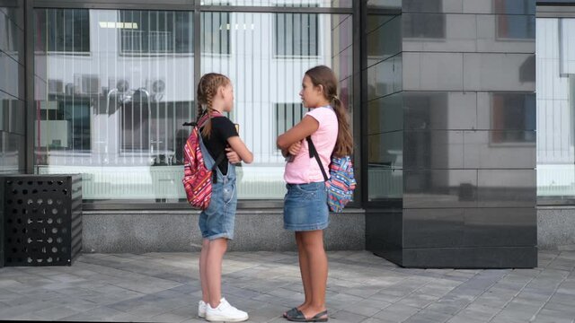  Two girls with backpack stand and talk together 