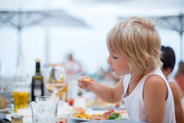 Sweet child, cute boy, eating pizza and french fries in a restaurant on the beach