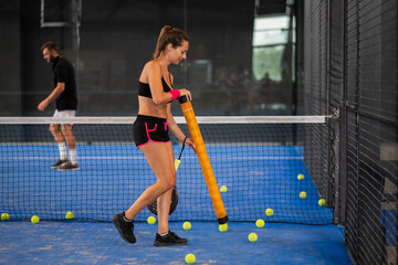 Girl collects padle or tennis balls in the middle of the court