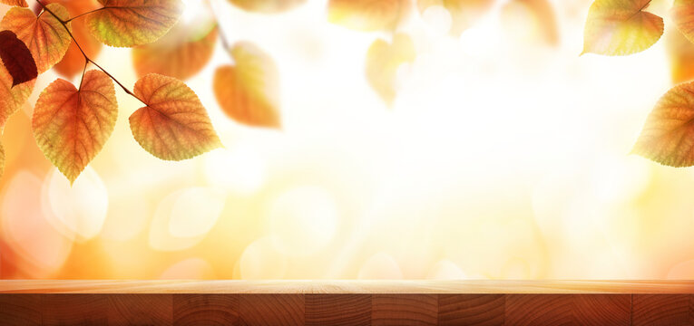 A wood table, tabletop product display with a golden autumn sunset sky and leaf background for seasonal, autumnal thanksgiving images.