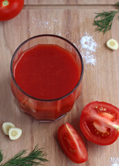 Fresh tomato juice in a glass with tomatoes, salt, garlic and herbs on a wooden board, top view