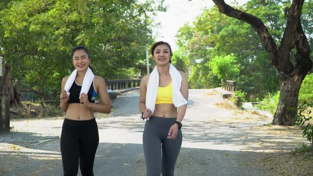 group of two friend fit asian women wearing sportswear with towel talking and walking after workout exercise or jog together in park outdoors . fit jogger  woman warm up to sport training in morning