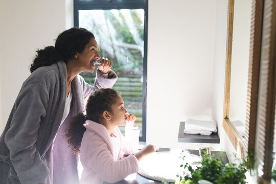 Midsection of mixed race mother and daughter brushing teeth in bathroom