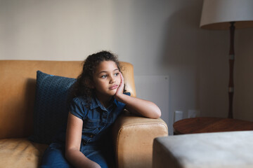 Mixed race bored girl sitting on sofa in living room