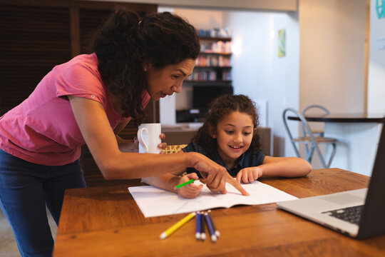 Mixed race mother holding coffee, helping her daughter do homework