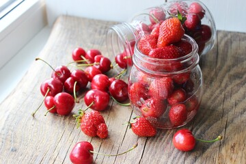 Ripe strawberries and cherries , glass jars. Wood background, rustic style. The concept of making jam, homemade preparations
