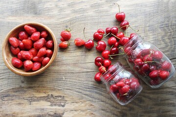 Ripe strawberries and cherries , glass jars. Wood background, rustic style. The concept of making jam, homemade preparations