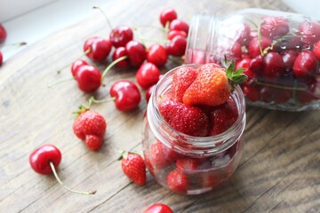 Ripe strawberries and cherries , glass jars. Wood background, rustic style. The concept of making jam, homemade preparations
