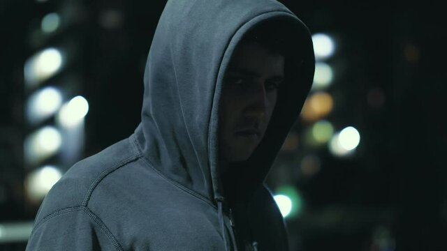 ugly mug - young hooded man looks at the camera in a threatening way - night 
