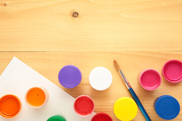 Multicolored jars of gouache and a brush on a light background. Creative kit.