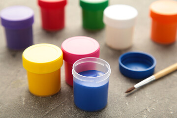 Multicolored jars of gouache and a brush on a grey background. Creative kit.