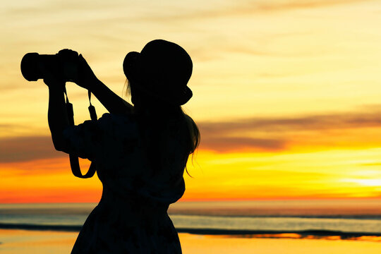 silhouette of woman tourist holding professional camera on nature landscape sunset