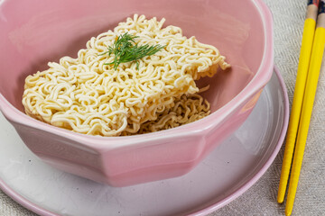 Quick instant dry noodles with parsley in pink bowl, Asian Chinese ramen pasta fast food eaten with yellow bamboo chopsticks