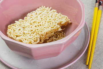 Quick instant dry noodles in pink bowl, Asian Chinese ramen pasta fast food eaten with yellow bamboo chopsticks