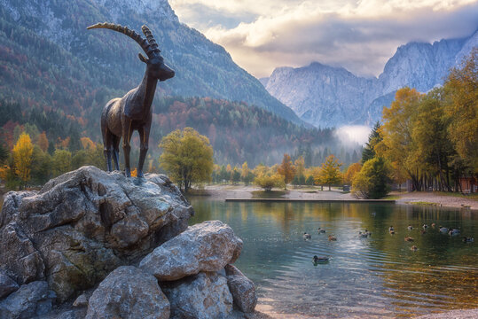 Kranjska Gora, Slovenia - October 18, 2019: Jasna lake in Triglav national park at sunrise, amazing autumn landscape with statue of Zlatorog, colorful trees and mountains, outdoor travel background