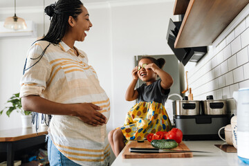 Black pregnant woman laughing and playing with her daughter in kitchen