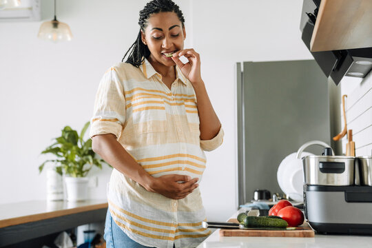 Black pregnant woman eating vegetable and holding her belly