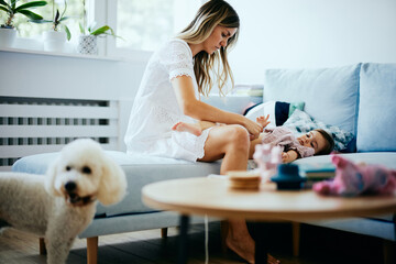 Young mother putting a diaper on her baby girl at home.