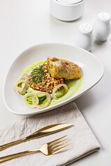 Turkey fillet with garnish and sauce. Baked turkey with bulgur, quinoa and vegetables. Restaurant dish. Copy space. Food styling and food photography. Table setting with cutlery. Light background