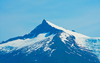 The top of the mountain is shaped like a pyramid. It is covered with melting snow. The fjords of Alaska, unique natural landscapes. Alaska, USA. June 2019.