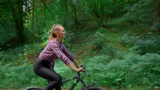 A young woman rides a bicycle through the forest. She enjoys the clean forest fresh air, gets high and enjoys life. happiness for a person. Rural areas and outdoor sports. Close-up
