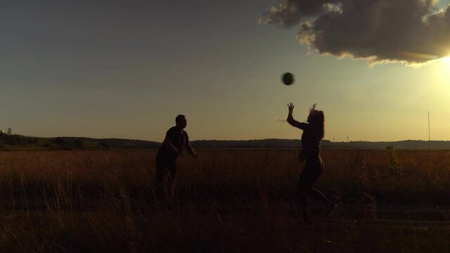 Three young energetic people are playing ball, volleyball at sunset on the field. Rural area, two girls and a guy. They have fun and have a great time. Youth and carelessness.