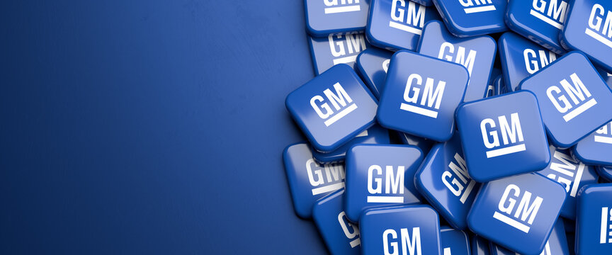 Logos of the US car manufacturer General Motors GM on a heap on a table. Copy space. Web banner format.