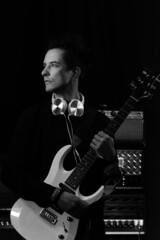 Black and white photo hipster guitar player with electric guitar and headphones in recording studio. Rock music concept. Portrait of confident heavy metal musician