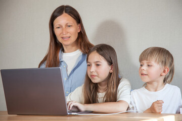 a siblings work on a laptop , their mother or teacher helps them. The concept of online or remote learning, homework