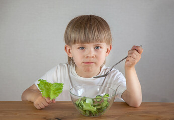 a boy with a sad face eats a salad of fresh green vegetables
