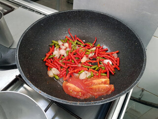 cooking the ingredients for making homemade Asian Traditional chilli sauce on a non stick frying pan in an stainless steel stove