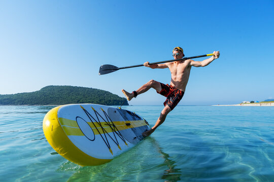 A man learns to stand on a board and falls into the water from a large yellow paddle board.