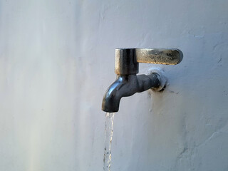 Water flows from stainless steel water taps mounted on white concrete walls in an urban house in the morning