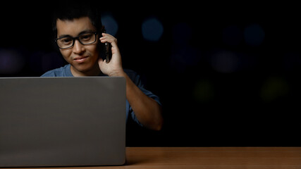 Young man with eye glasses using a smartphone and computer laptop at home, work from home concept.