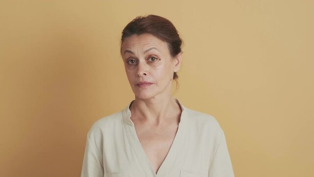 A smiling middle-aged brunette woman nodding something standing isolated over beige background in the studio