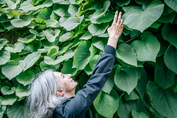 Woman reaches hand up against the background of a wall of foliage