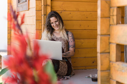 Female working on her laptop, on a balcony of a log cabin in the woods