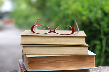 Stack of vintage books and reading glasses in a garden. Selective focus.
