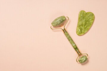 Jade roller and gua sha stone massager at pastel background. Anti-aging therapy. Top view.