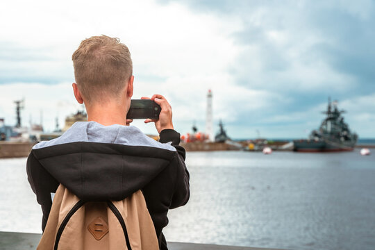 A man takes photos with a smartphone of warships in Kronstadt in cloudy weather
