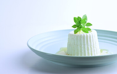 Close up, fresh cheese with honey on a plate, topped with a small sprig of basil. Light background and copy space.