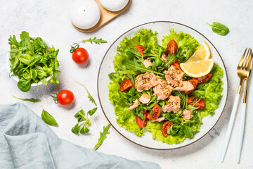 Salad with baked salmon fish. Green salad mix with tomatoes and salmon. Top view at white table.