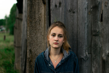 Portrait of a young girl with anxious face at sunset in the countryside on against a wooden barn
