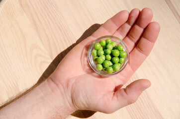 Hand with green pea in glass bowl of top view on rustic wooden background